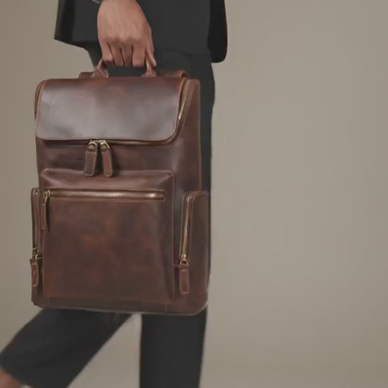 Man in a suit carrying the brown Crazy Horse leather flap laptop backpack by its top handle