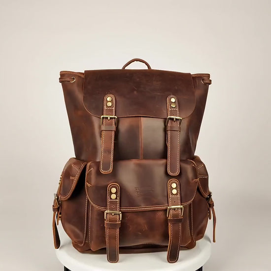 Brown leather drawstring buckle rucksack turning on a stand, showing the front buckle pockets and flap